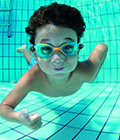 Pojke med simglasögon som simmar undervattnet i en simbassäng