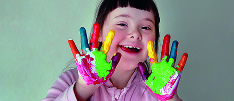 Flicka som ler och visar upp händer fyllda med färg