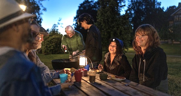 Personer sitter utomhus vid bord med fotogenlykta, bild