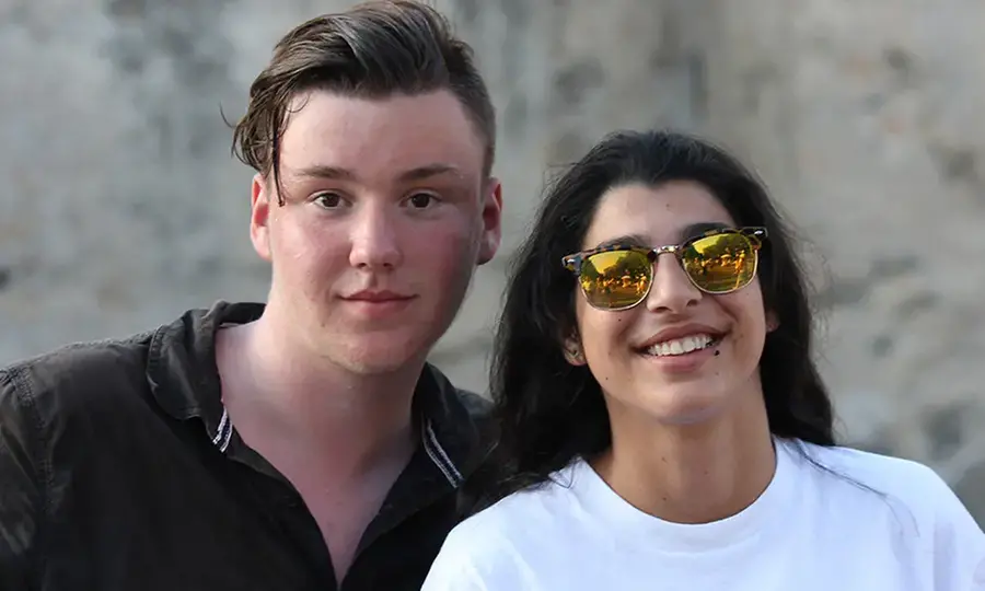 Två ungdomar, en pojke och en flicka, tittar in i kameran. Flickan har ett par solglasögon på sig.