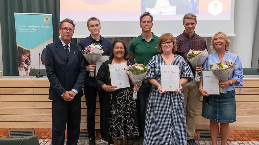 Sju personer står uppställda framför stor bildskärm vid prisceremoni för årets lärare och ledare i Sundbybergs stad. Några håller diplom i handen.